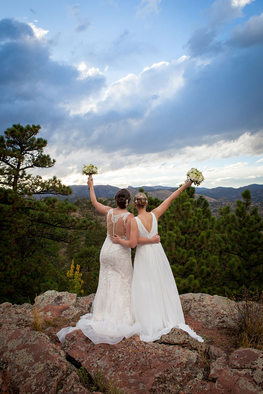 two brides looking out at mountains holding up bouquets