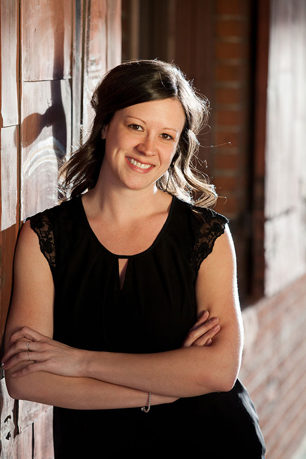 Girl leaning against brick wall with arms crossed in black shirt looking at camera